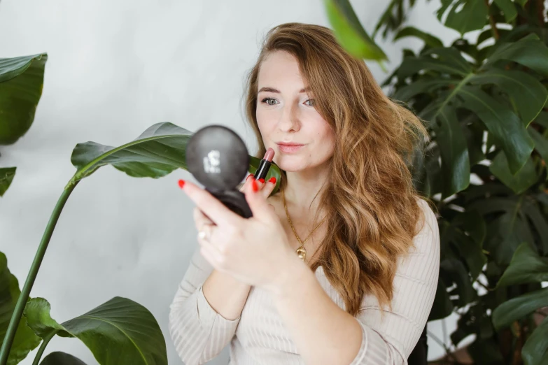 a woman holding a hair dryer in front of her face, a picture, by Julia Pishtar, trending on pexels, coral lipstick, next to a plant, profile image, holding flask in hand