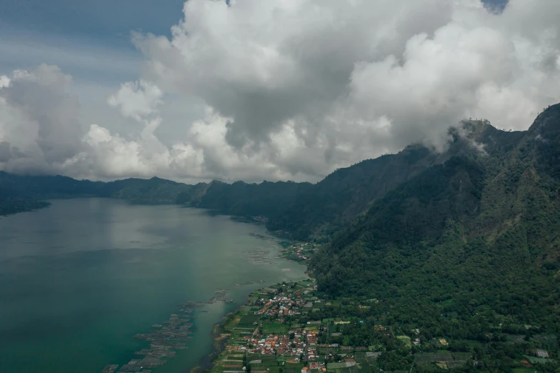 a large body of water next to a lush green hillside, by Daren Bader, pexels contest winner, sumatraism, clouds and corrupted city behind, boka, joel sternfeld, airborne view