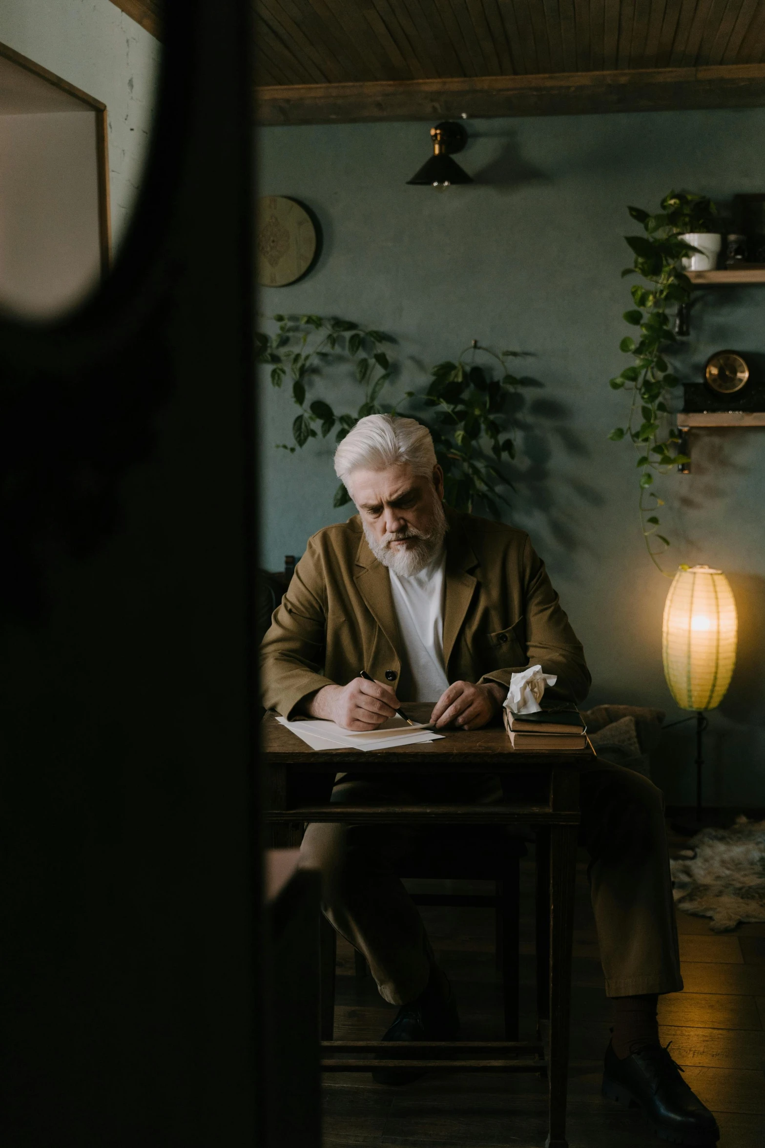 a man sitting at a table writing on a piece of paper, silver hair and beard, jovana rikalo, high quality photo, abcdefghijklmnopqrstuvwxyz