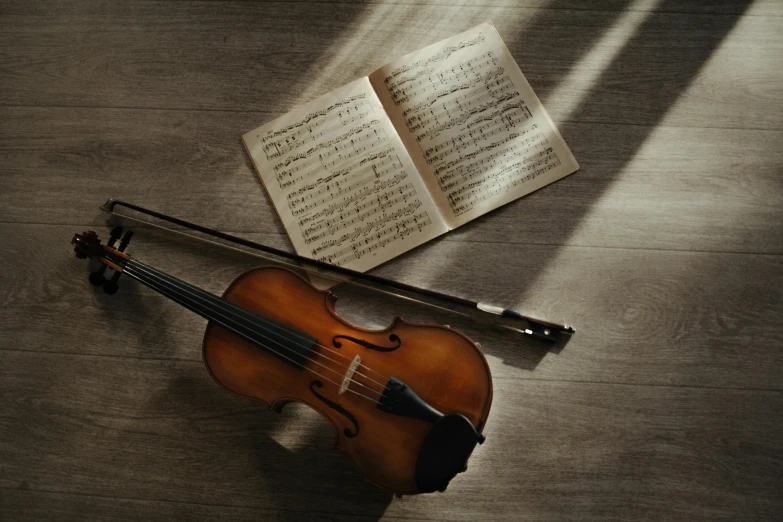 a violin sitting on top of a wooden floor next to a book, thumbnail, light and dark, list, afternoon