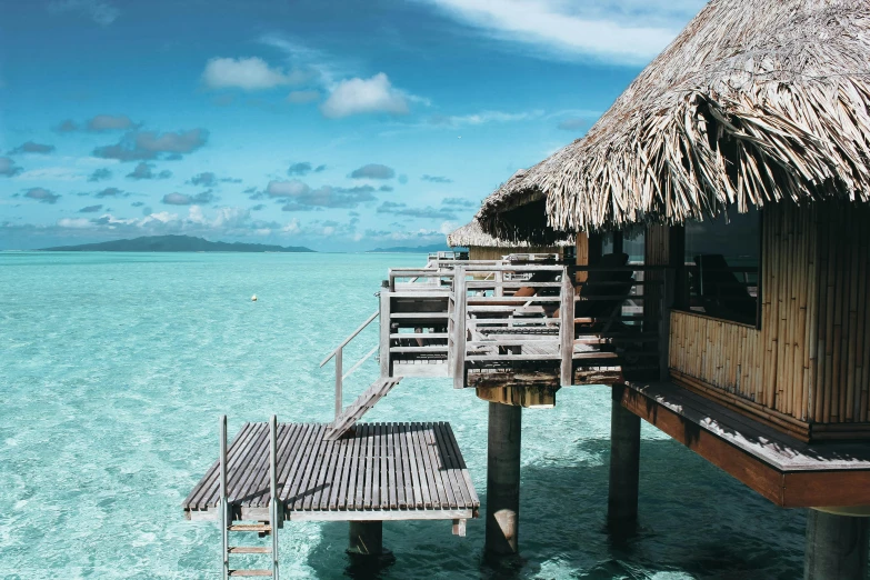 a thatched hut sitting on top of a body of water, on the ocean, balcony, turquoise water, exterior