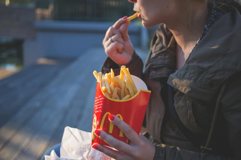 a woman sitting on a bench eating french fries, inspired by Elsa Bleda, pexels, photorealism, eating inside mcdonalds, red stripe, people outside eating meals, crisps