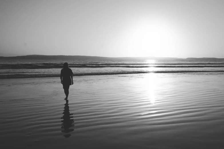 a black and white photo of a person walking on the beach, water reflecting suns light, 4k greyscale hd photography, near the seashore, golden hour photo