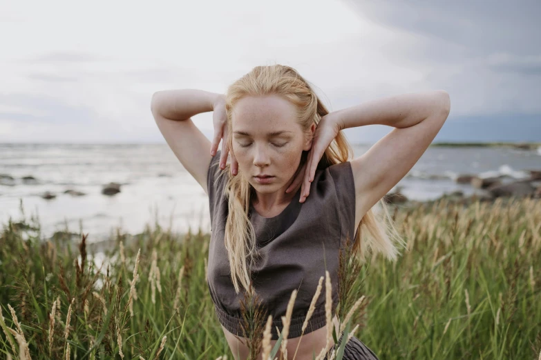 a woman standing in tall grass next to a body of water, inspired by Louisa Matthíasdóttir, unsplash, hands in her hair, eleanor tomlinson, wearing a crop top, various posed