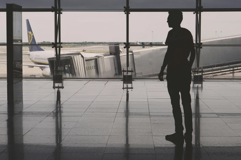 a man standing in front of a window at an airport, by Emma Andijewska, pexels contest winner, happening, lone silhouette in the distance, standing in an arena, julian opie, featured art