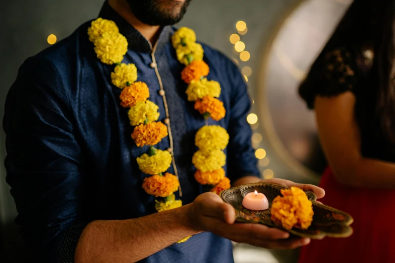 a man holding a lit candle in his hand, trending on unsplash, hurufiyya, dressed in a jodhpuri suit, marigold flowers, wearing jewellery, indigo