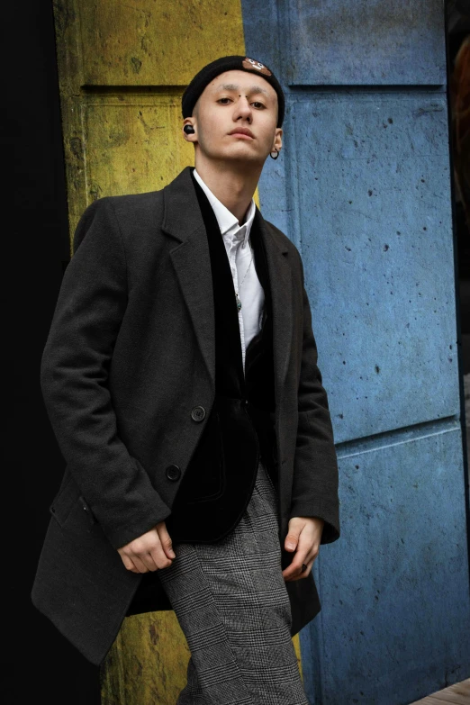 a man in a suit and tie standing in front of a building, an album cover, inspired by Itō Ogura Yonesuke, trending on pexels, bauhaus, grey tarnished longcoat, portrait androgynous girl, ( side ) profile, non binary model