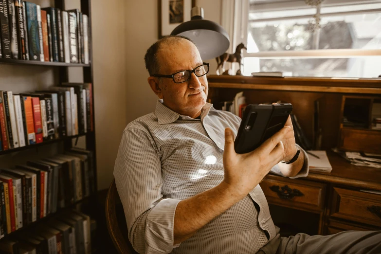 a man sitting in a chair holding a tablet computer, a portrait, by Will Ellis, pexels contest winner, happening, wearing reading glasses, australian, at home, thumbnail