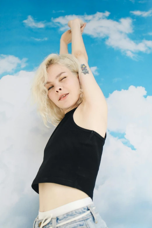 a woman with her arms up in the air, an album cover, inspired by Elsa Bleda, trending on pexels, magic realism, tattoos of cumulus clouds, pale skin curly blond hair, wearing a cropped black tank top, elle fanning)