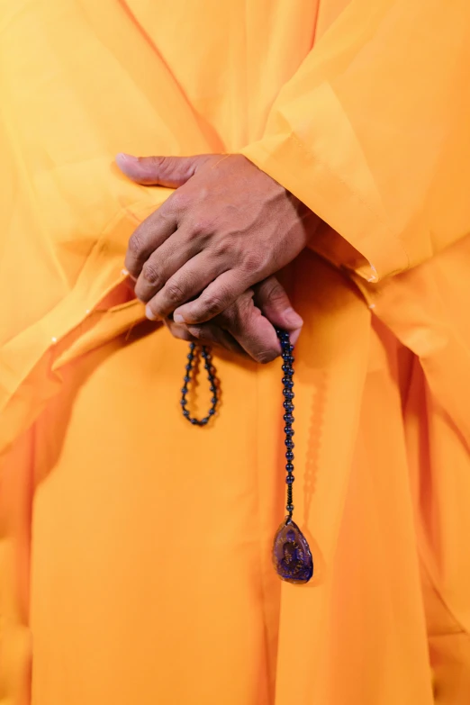 a person in a yellow robe holding a rosary, by Bernard Meninsky, unsplash, minimalism, wearing orange prison jumpsuit, buddhist monk, photograph credit: ap, closeup of arms