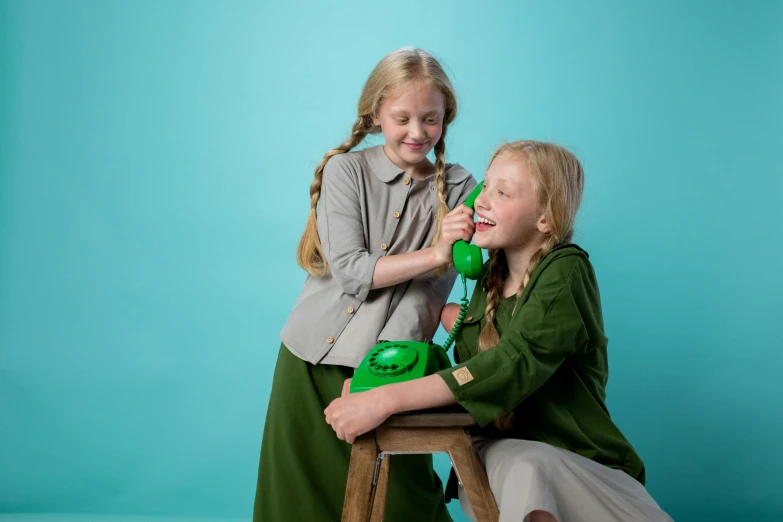 a couple of girls sitting on top of a wooden chair, inspired by Elsa Beskow, wearing green jacket, girl making a phone call, official product photo, cast