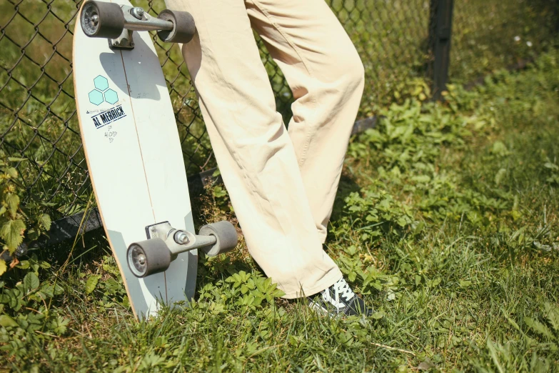 a man leaning on a skateboard next to a fence, happening, green corduroy pants, soft white rubber, chillwave, zoomed in