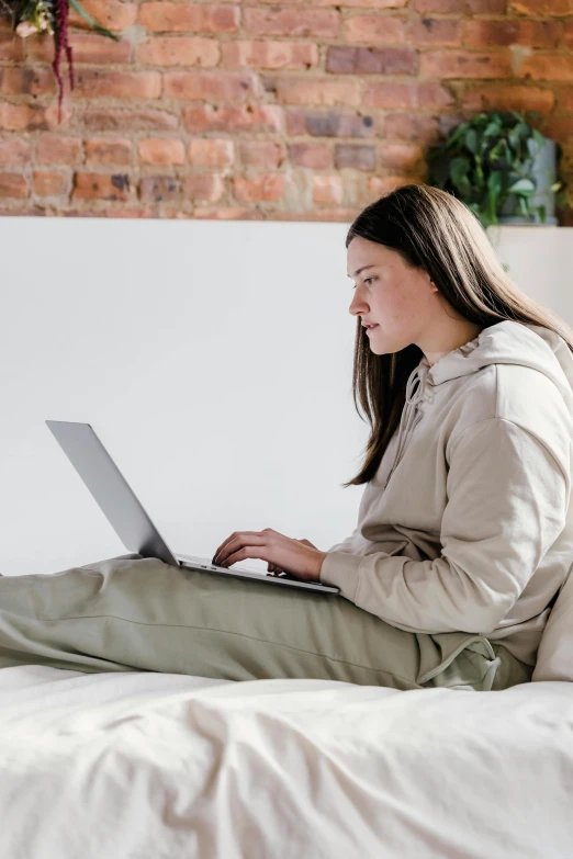 a woman sitting on a bed using a laptop, trending on pexels, renaissance, beige hoodie, profile image, technical, laying down