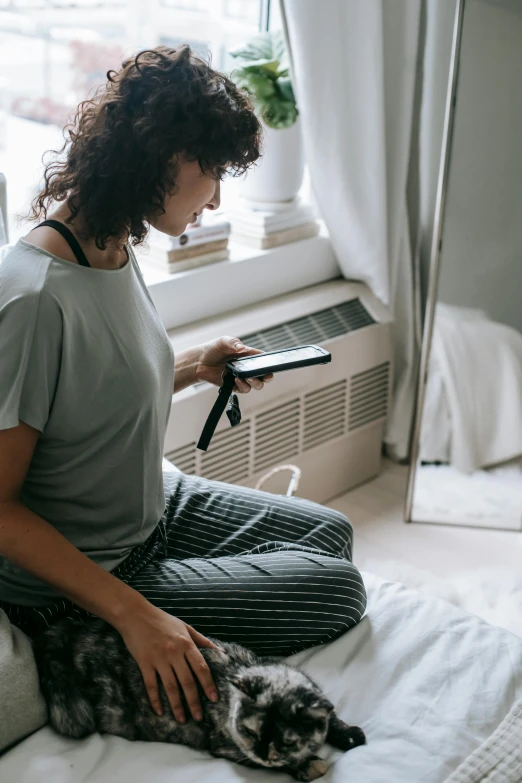 a woman sitting on a bed petting a cat, trending on pexels, happening, looking at his phone, curly haired, watching tv, cooling