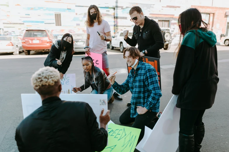 a group of people sitting on the side of a road, a photo, pexels, graffiti, subject action : holding sign, group sit at table, ashteroth, hollywood standard