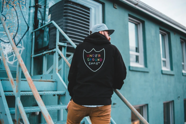 a man standing on the steps of a building, inspired by Okuda Gensō, unsplash contest winner, graffiti, black hoodie, back view, patch logo design, owen gent