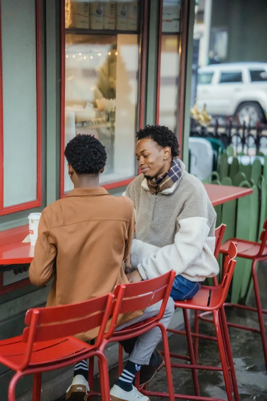 two men sitting at a table outside of a restaurant, trending on pexels, lesbian embrace, african american woman, wearing a red turtleneck sweater, android coffee shop