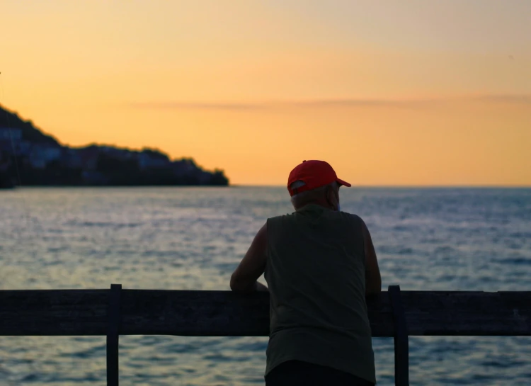 a man sitting on a bench looking out at the ocean, pexels contest winner, orange hue, florida man, people watching, looking old