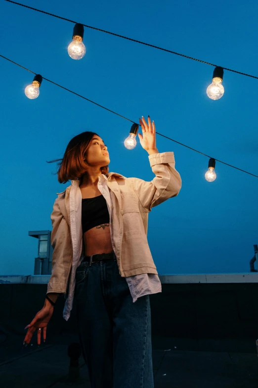 a woman standing on top of a roof next to a string of lights, trending on pexels, wearing a crop top, cropped shirt with jacket, a young asian woman, play of light