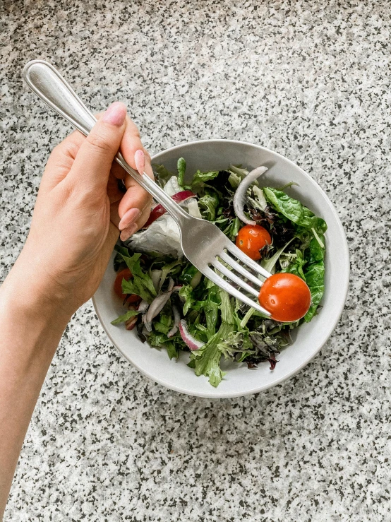 a person eating a salad with a fork, high quality product image”, silver small small small glasses, hands on counter, grey