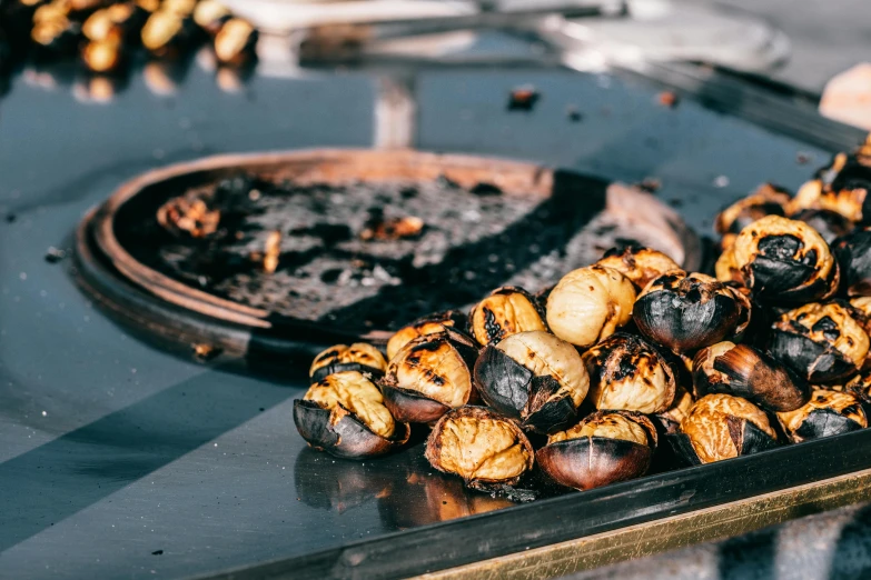 a tray filled with roasted chestnuts on top of a table, by Julia Pishtar, trending on unsplash, grilled artichoke, charred desert, on a sunny day, tanjiro kamado