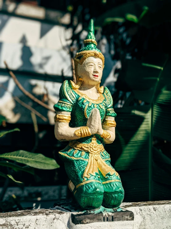 a statue sitting on top of a cement wall, inspired by Lam Qua, unsplash, green and gold, thai, sitting in the garden, made of glazed