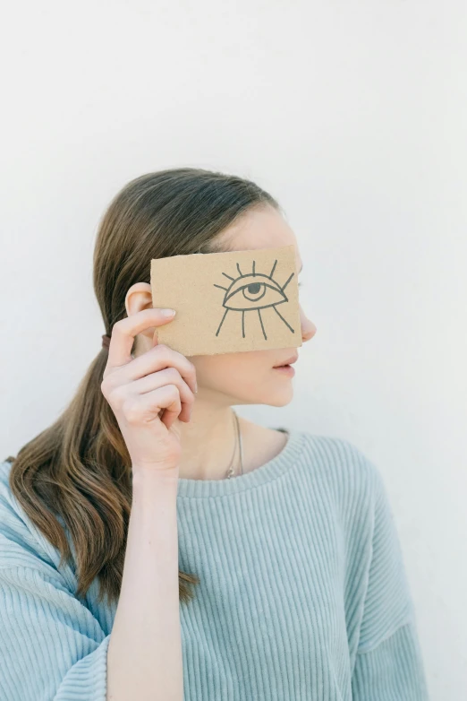 a woman holding a piece of cardboard with an eye drawn on it, inspired by Saul Steinberg, trending on pexels, psychic girl, soft aesthetic, made of cardboard, profile pic