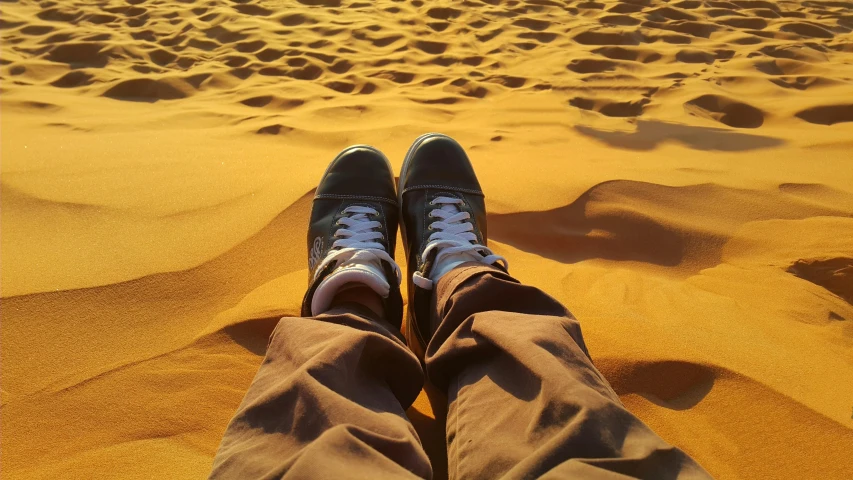 a person sitting on top of a sandy beach, a picture, pexels contest winner, hyperrealism, sneakers, sahara desert, in front of an orange background, deep golden sand desert
