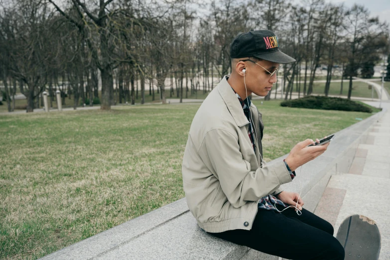 a man sitting on a ledge looking at his cell phone, trending on pexels, ashteroth, in a park, non-binary, alexey gurylev