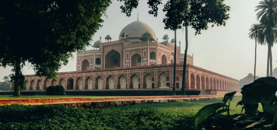 a large building sitting on top of a lush green field, a colorized photo, inspired by Steve McCurry, pexels contest winner, renaissance, white sweeping arches, indian patterns, dome, 1980s photo