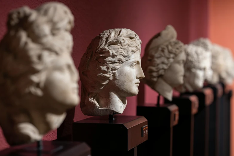 a row of statues sitting on top of a wooden table, a marble sculpture, trending on pexels, neoclassicism, head shot, alexander the great, museum quality photo, curls