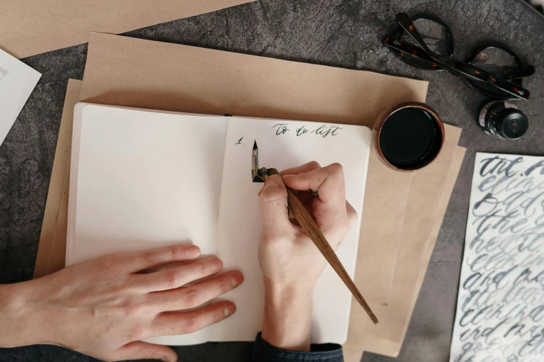 a person writing on a piece of paper with a pen, pexels contest winner, visual art, calligraphic poetry, background image, cardboard, flatlay