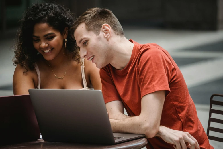 a man and a woman sitting at a table looking at a laptop, trending on pexels, lachlan bailey, college girls, background image