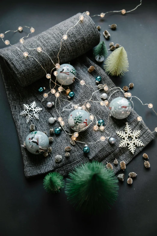 a bunch of ornaments sitting on top of a table, a portrait, dramatic product lighting, hues of subtle grey, made of felt and cloth and beads, evergreen branches