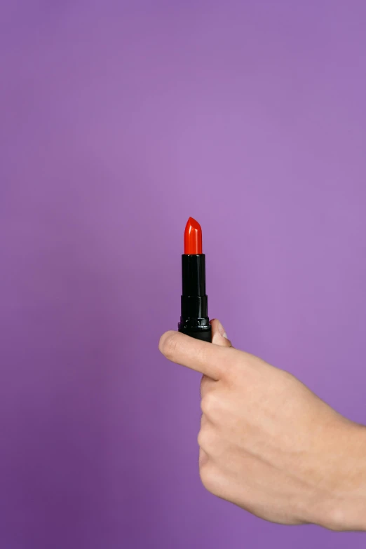 a person holding a red lipstick in their hand, some purple and orange, zoomed out shot, dramatic product shot, red - black