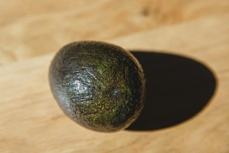 an avocado sitting on top of a wooden table, inspired by Grillo Demo, hurufiyya, iridescent titanium, dynamic angled shot, frontal shot, medium angle