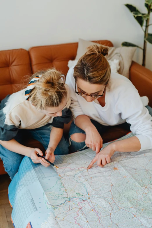 a woman and a child sitting on a couch looking at a map, by Jessie Algie, pexels, fine art, college girls, head straight down, two buddies sitting in a room, on a canva