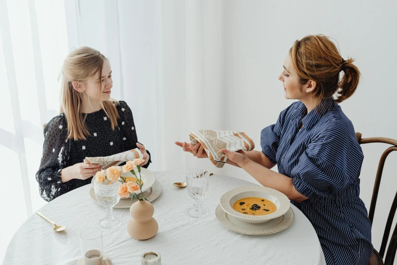 two women sitting at a table with plates of food, by Liza Donnelly, pexels contest winner, in a white boho style studio, with a kid, angelina stroganova, gif