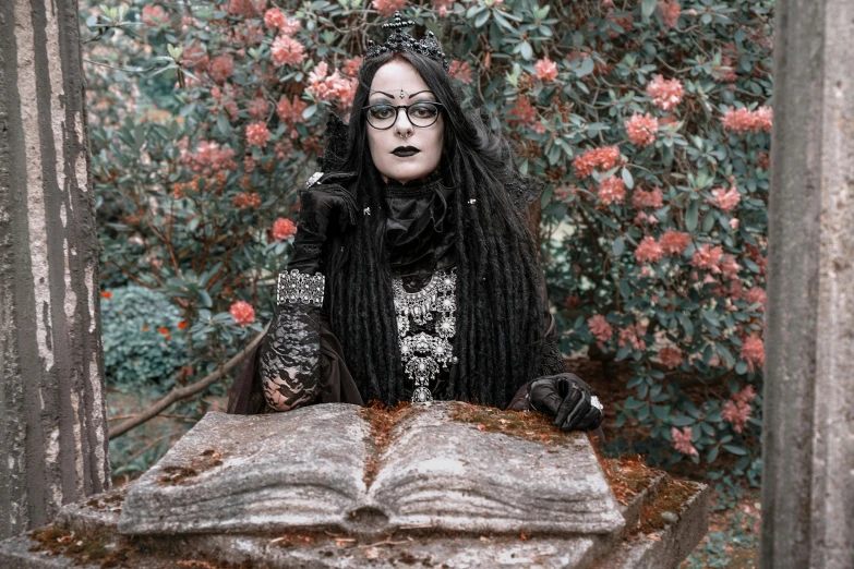 a woman sitting at a table with an open book, an album cover, inspired by Louis Grell, pexels contest winner, gothic art, goddess of death in a graveyard, covered in runes, portrait mode photo, black rococo