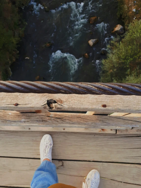 a person standing on a wooden platform next to a river, looking down from above, 8 feet fall, very comfy], up close