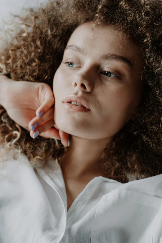 a woman with curly hair laying on a bed, a portrait, trending on pexels, hand on her chin, iridescent skin, neck zoomed in, fashion model portrait