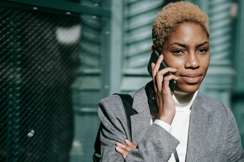 a close up of a person talking on a cell phone, trending on pexels, afrofuturism, woman in business suit, short curly blonde haired girl, androgynous male, posed