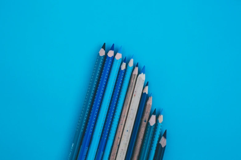 a group of pencils sitting next to each other on a blue surface, a stipple, trending on unsplash, visual art, fan favorite, penned in cyan ink, multiple stories, blue and white colour scheme