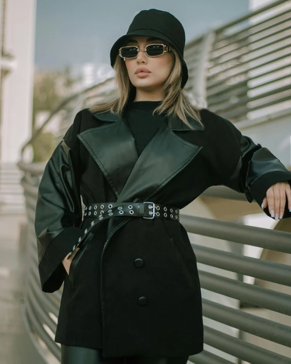 a woman in a black coat and hat posing for a picture, by Robbie Trevino, wearing studded leather, estefania villegas burgos, detailed product image, low quality photo