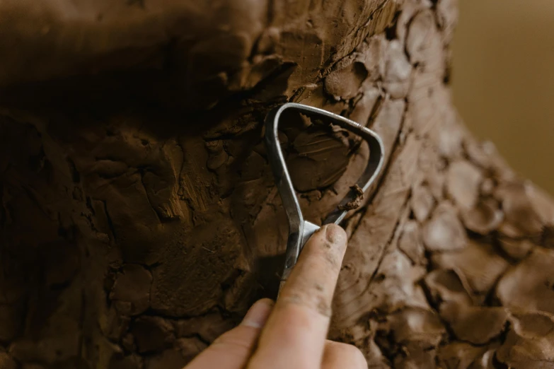 a close up of a person holding a pair of scissors, an abstract sculpture, by Thomas Furlong, pexels contest winner, chocolate frosting, found in a cave made of clay, trees growing on its body, fine texture detail