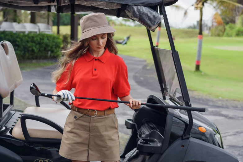 a woman standing next to a golf cart, pexels contest winner, orange shoulder pads, wearing polo shirt, baggy clothing and hat, top down shot