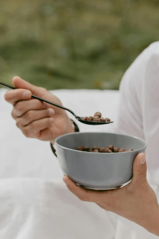 a close up of a person holding a bowl of food, a digital rendering, unsplash, morning detail, grey, chocolate, eating outside