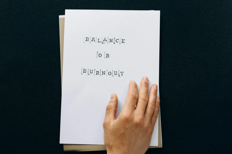 a person holding a book on top of a table, an album cover, by Elizabeth Durack, pexels contest winner, burnout, hand drawn type, balance, sheet of paper