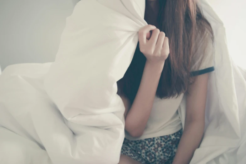 a woman sitting on top of a bed under a blanket, shy, wearing a white blouse, girl wearing hoodie, korean woman