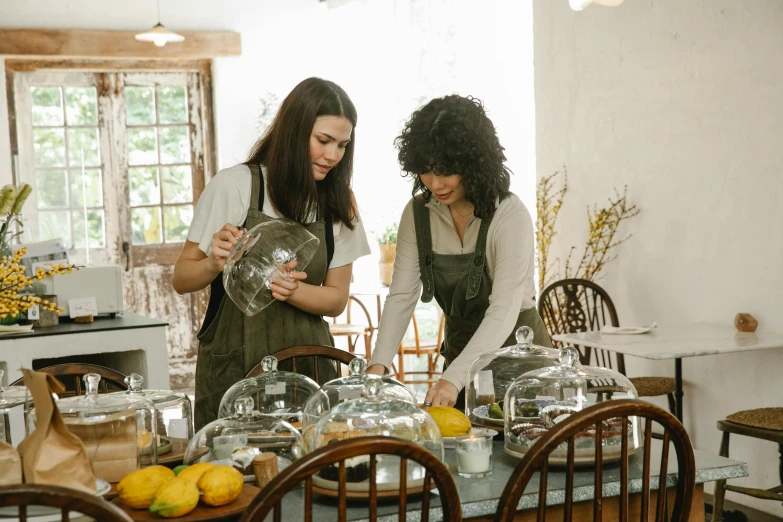 a couple of women standing next to each other at a table, by Jessie Algie, pexels, cottagecore, glass domes, breakfast, serving body